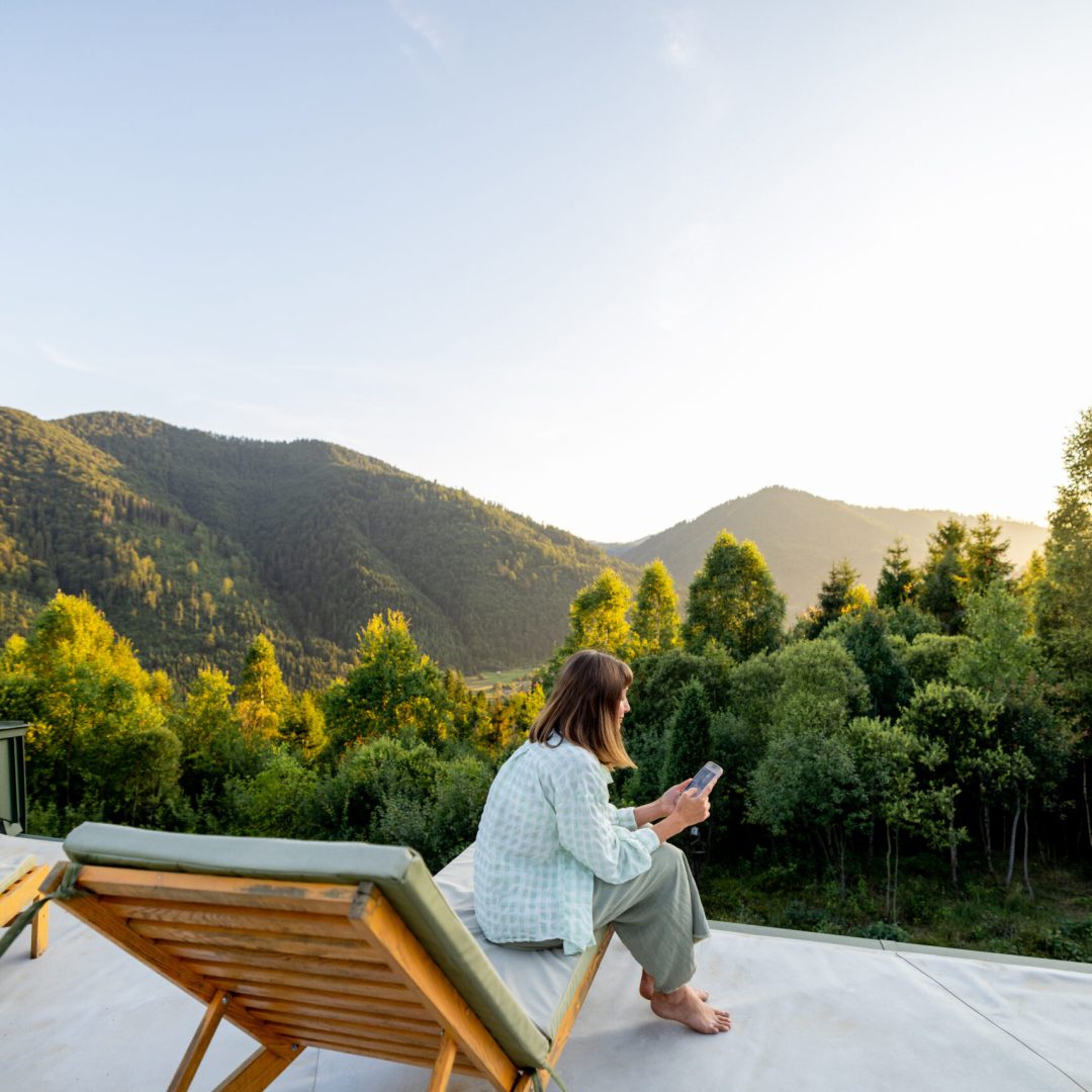 A woman enjoys the morning sun on a rooftop while using her phone, embracing the tranquility of nature with the convenience of modern technology