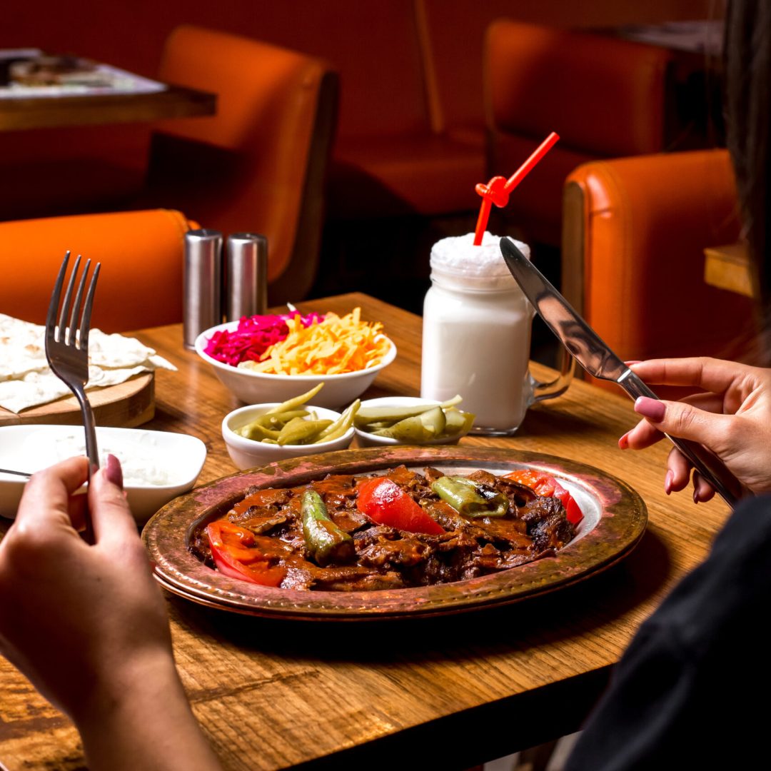 woman is served iskender kebab in copper platter with pickles yogurt and ayran vertical